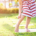 A child itching their leg with mosquitos swarming around them.